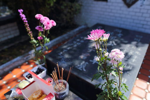 Offerings, bouquets of flowers and burning incense in front of the grave