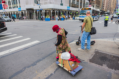 New York. USA. 09.19.2022. Close-up view of homeless woman with belongings on cart crossing street at crosswalk in Manhattan,