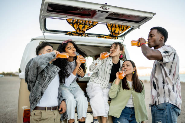 Group of young friends drinking soda on the trunk of a van outdoors