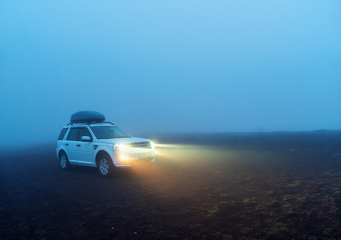 Russia. Karachay-Cherkessia, Shajatmaz plateau. October 2022. Soft focus. Poor weather visibility. White travel car in the night fog with its headlights on on the edge of a cliff. Lost in a thick fog.