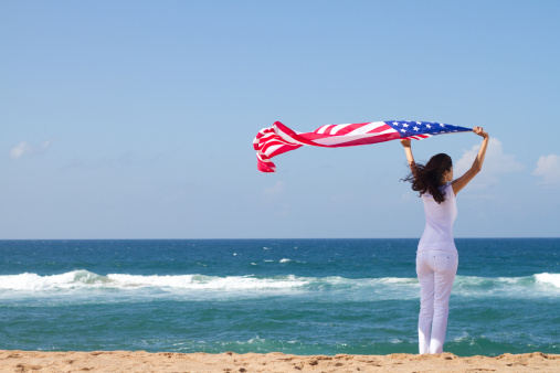 american dream concept: young woman holding american flag on beach