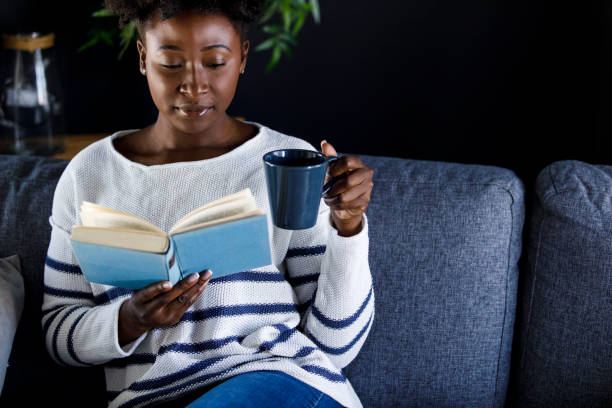istock Young woman relaxing on the sofa, enjoying coffee and reading a book 1467593437