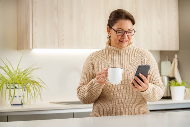 istock Woman having coffee and using smart phone in kitchen 1467593955