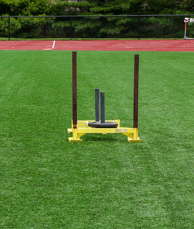 One yellow sled with a twenty five pound weight ready to be pushed on a turf field for strength.