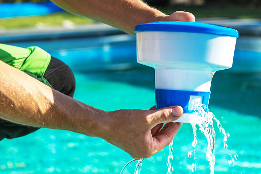 Closeup of Floating Chemical Dispenser in Hands of Professional Swimming Pool Technician During Scheduled Maintenance.