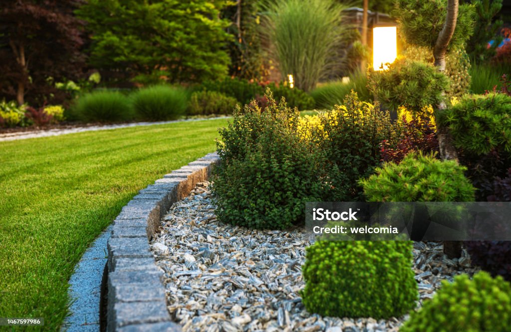 Professionally Landscaped Garden Flower Bed Closeup of Professionally Landscaped Flower Bed with Decorative Green Garden Plants and Evenly Mowed Lawn in the Background. Landscaped Stock Photo
