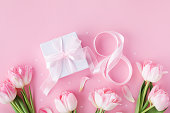 Spring background with bouquet of tulip flowers and gift box on pastel pink table top view. Greeting card for 8 March International Women Day. Flat lay.