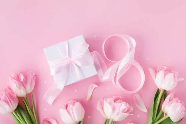 Spring background with bouquet of tulip flowers and gift box on pastel pink table top view. Greeting card for 8 March International Women Day. Flat lay style.