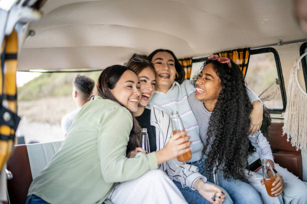istock Girlfriends embracing while drinking soda on retro mini van transport 1467599868
