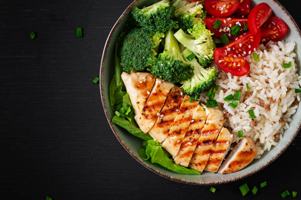 Delicious buddha bowl with grilled chicken, fresh vegetables and rice on a dark background. Top view, above