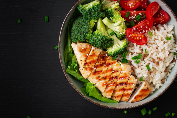 Delicious buddha bowl with grilled chicken, fresh vegetables and rice on a dark background. Top view, above stock photo