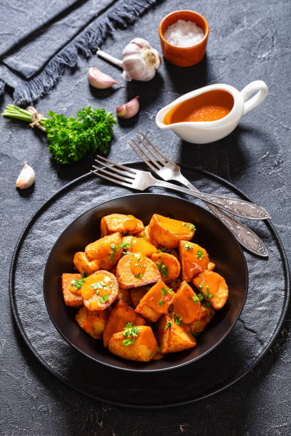 patatas bravas, deep fried potatoes with sauce patatas bravas, deep fried potatoes with spicy sauce in black bowl on concrete table, spanish cuisine, vertical view patatas bravas stock pictures, royalty-free photos & images