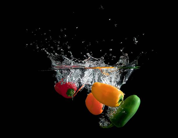 Four Bell Peppers falling into water splashing against black stock photo