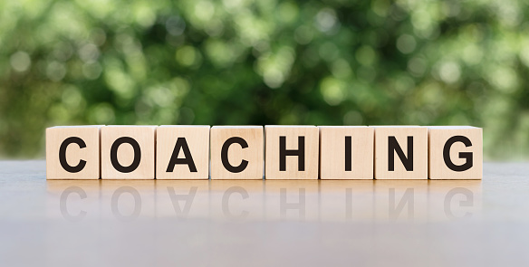 COACHING. Word written on wooden blocks. The text is written in black letters and is reflected in the mirror surface of the table. Business concept for your design.