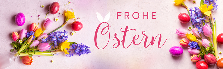 Colorful signs of spring for happy easter greetings on tender pink. Horizontal background for greeting cards and banner with german text. Top view.