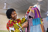 Smiling Ghanaian Dressmaker with African pattern dress in her studio