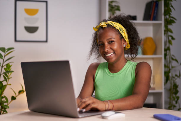 Young African woman using laptop home office. Beautiful cheerful girl poses looking camera. stock photo