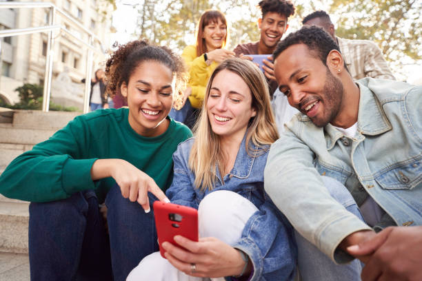 istock Group of young people watching something at and using phone sitting on stairs. Students lifestyle 1467623339