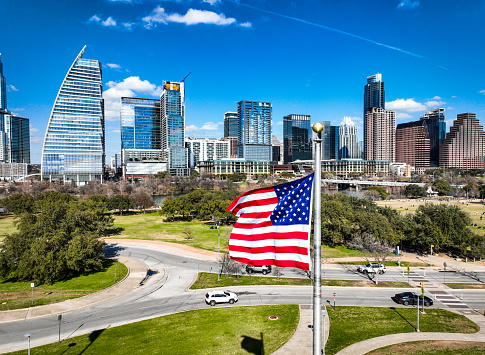 American Flag with red and white streets and 50 stars flies in front of the Austin Texas USA skyline cityscape on a sunny afternoon in the Capital City of Texas