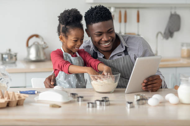 istock Happy black father and daughter baking together, using digital tablet 1467628319