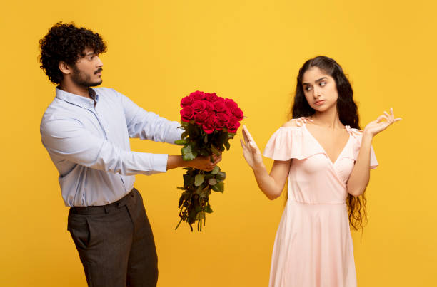 confessione indesiderata. signora indiana dispiaciuta che rifiuta il suo ammiratore con le rose il giorno di san valentino, sfondo giallo - valentines day love nerd couple foto e immagini stock