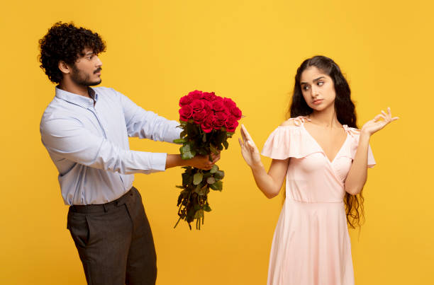 unwanted confession. displeased indian lady rejecting her admirer with roses on valentine's day, yellow background - valentines day love nerd couple imagens e fotografias de stock