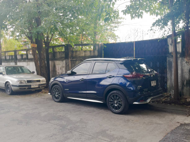 Blue Nissan Kicks electric vehicle is parked in street along wall with gate under trees in residential district in  Bangkok Chatuchak