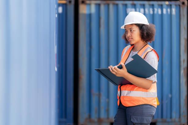 istock African American dock manager in uniform and safety helmet working and inspector at container cargo take some note on clipboard. Logistics import and export shipping yard. Transportation and global business concept 1467631333