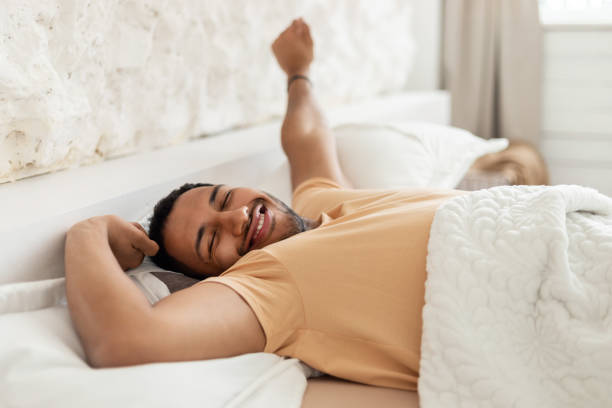 szczęśliwy arabski mężczyzna budzący ziewanie wyciągające ramiona leżące w sypialni - pillow wake up yawning sleeping zdjęcia i obrazy z banku zdjęć