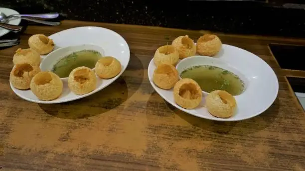 Two plates of Pani Puri or Golgappa or Puchkas from a white plate which is popular Indian Chat menu.