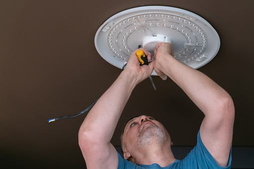 A man installs a chandelier on the ceiling