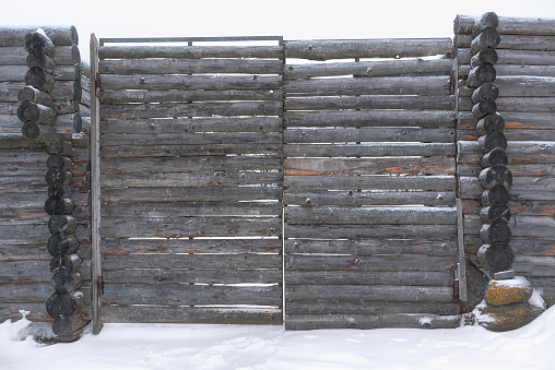 Vintage wooden gate made of darkened boards. Trampled snow in front of the gate.