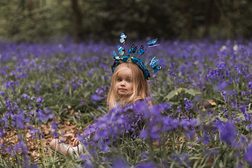 Child with bluebells. Little girl in pretty dress playing in beautiful spring forest with purple bluebell flowers. Kids hiking in park with blue bell flower meadow. Preschooler exploring nature
