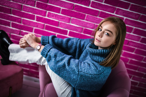 Cute Female Sitting On Chair In Front Of Pink Brick Wall