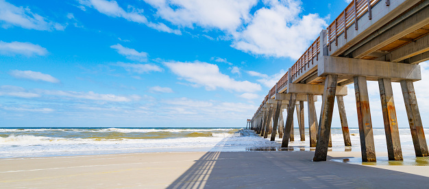Seascape with sunny white sand beach, cloudy blue sky, shadows, and JAX  Beach Fishing Pier in Jacksonville, North Florida, USA