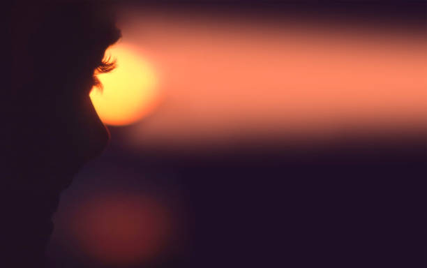 The eyelashes of a woman are silhouetted against the setting sun.