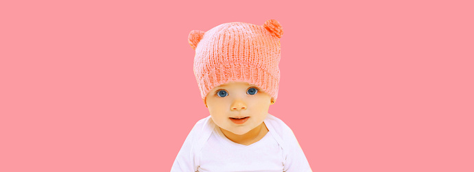 Portrait close up of cute smiling baby in pink knitted hat with bear ears on background