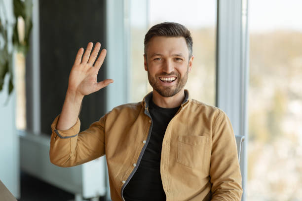 istock Joyful Businessman Waving Hello Smiling To Camera Sitting In Office 1467665143