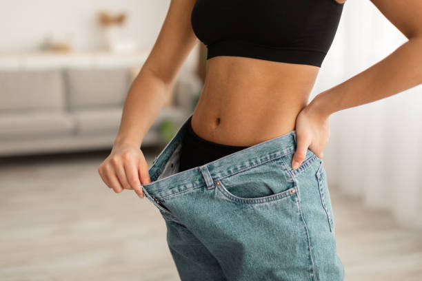 unrecognizable black lady showing abdominal muscles wearing oversized jeans indoor - torso women jeans abdomen imagens e fotografias de stock