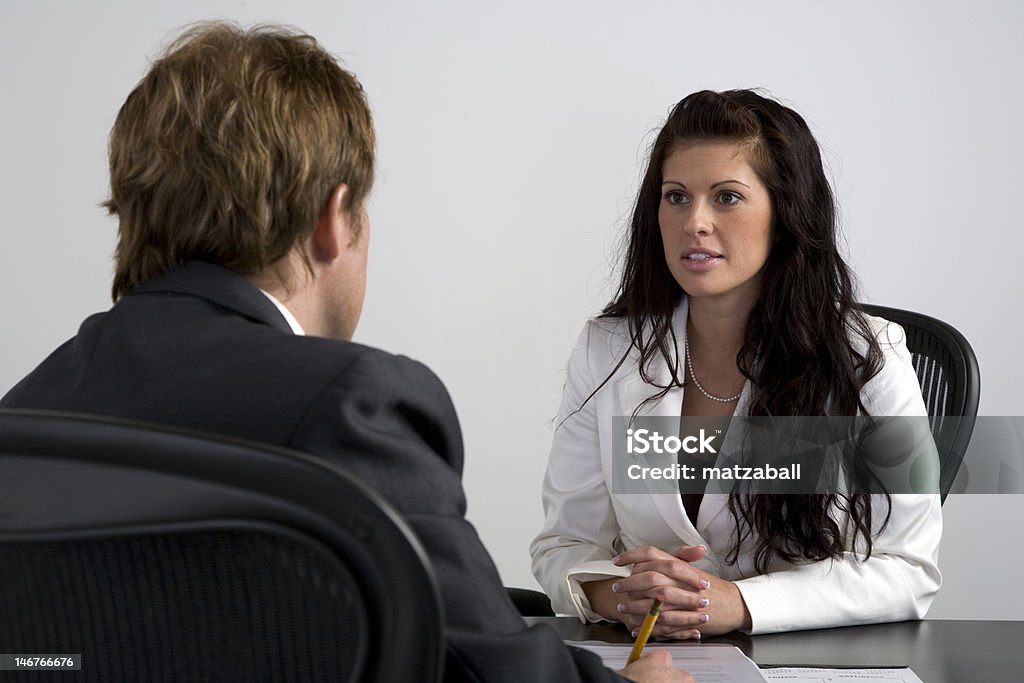 Job Review A young business woman sits in an office setting as she is being interviewed/having a performance review with a male colleague. Job Interview Stock Photo