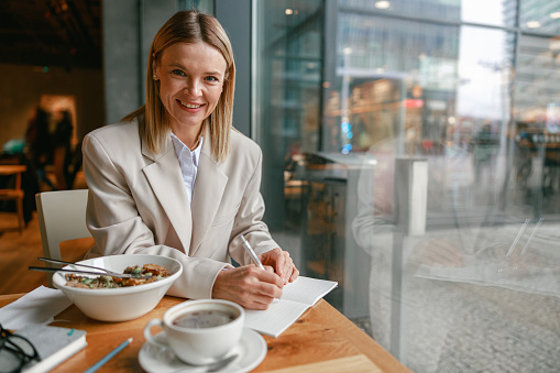 Smiling businesswoman having lunch and making notes while working in cafe. High quality photo