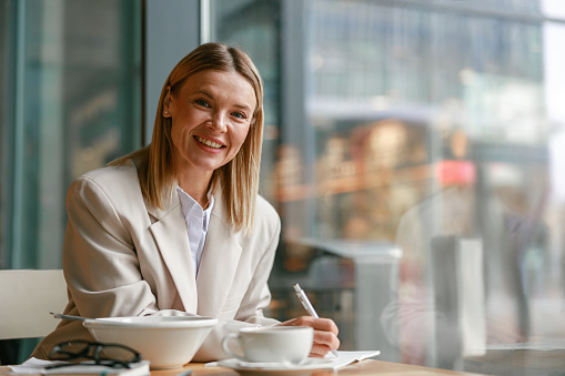 Smiling businesswoman having lunch and making notes while working in cafe. High quality photo