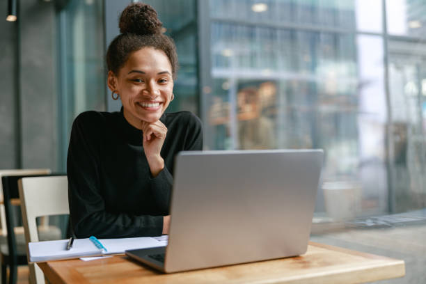 istock Smiling female student studying on laptop while sitting in cafe and looking on camera 1467670436