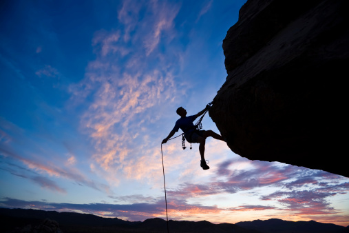 A rock climber is silhouetted against the evening sky as he rappels past an overhang in Joshua Tree National Park.