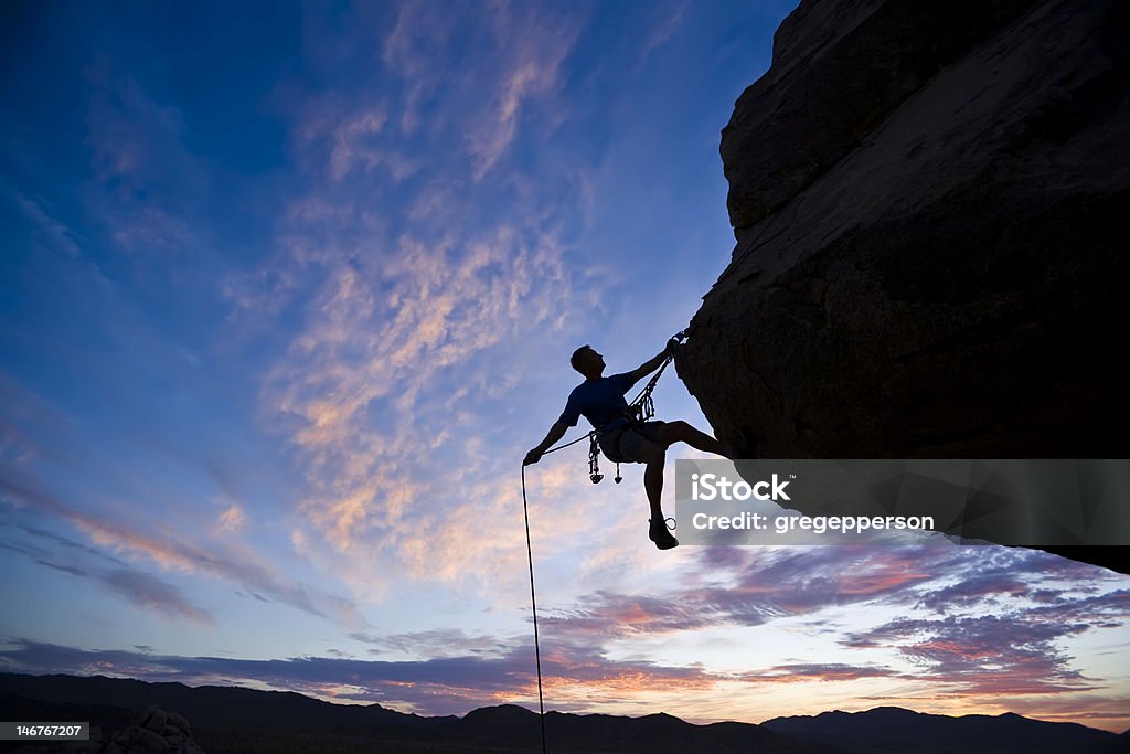 Rock climber against an evening sky A rock climber is silhouetted against the evening sky as he rappels past an overhang in Joshua Tree National Park. Rock Climbing Stock Photo