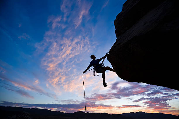 Rock climber against an evening sky A rock climber is silhouetted against the evening sky as he rappels past an overhang in Joshua Tree National Park. rock climbing stock pictures, royalty-free photos & images