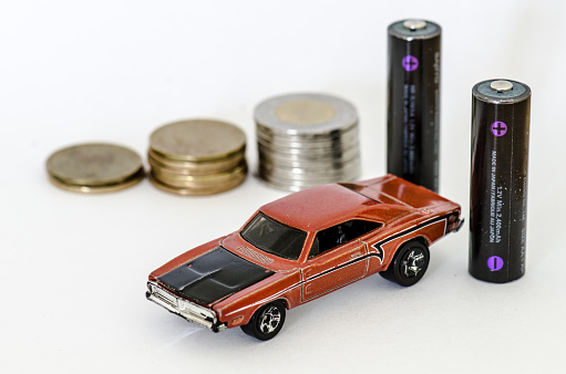 Miniature car with two AA batteries and pile of coins behind on white background
