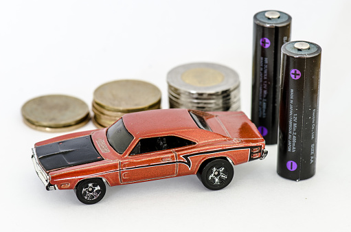 Miniature car with two AA batteries and pile of coins behind on white background