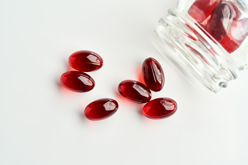 Red krill oil pills or globules with a glass bottle on white background, top view