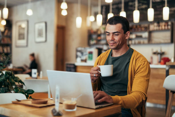 Mature man working remotely on laptop from cafe and drinking coffee during video call